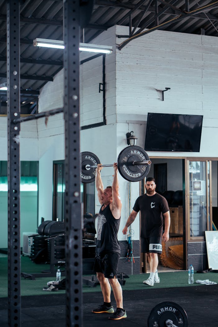 about-bg A man lifting a barbell in a modern gym with gym equipment in the background.