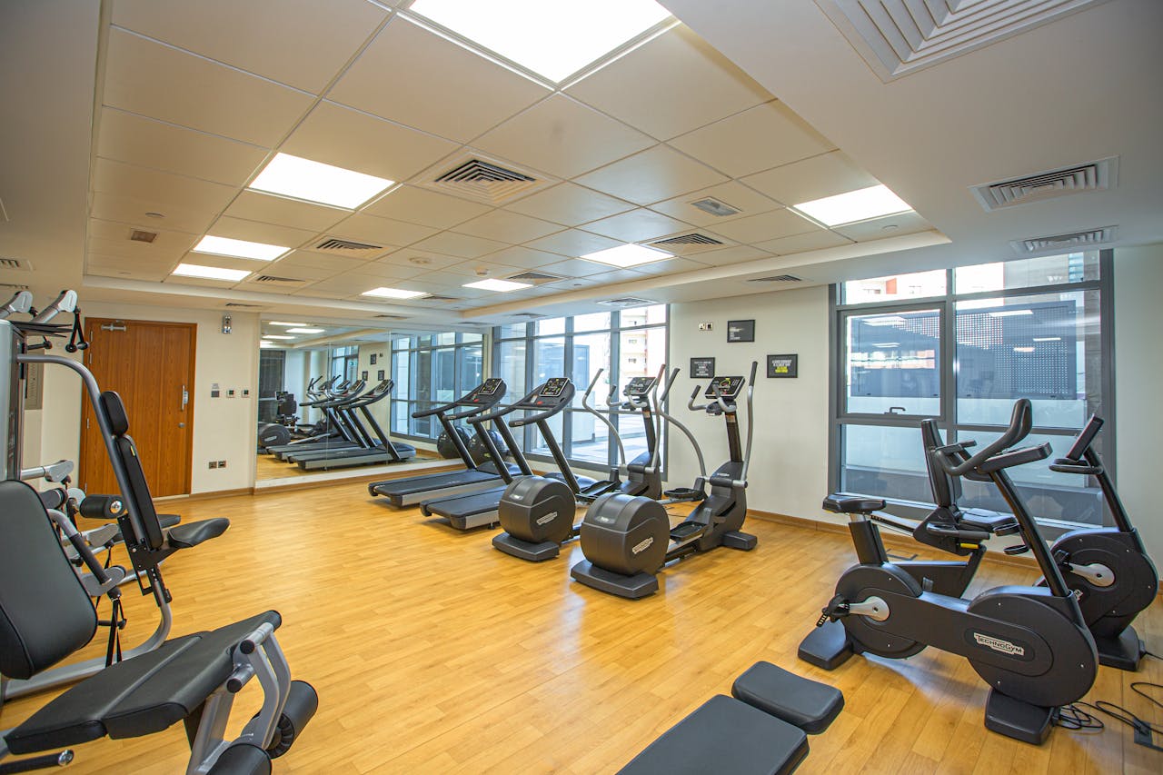 who-we-are Spacious indoor gym with treadmills, stationary bikes, and exercise equipment on a wooden floor.